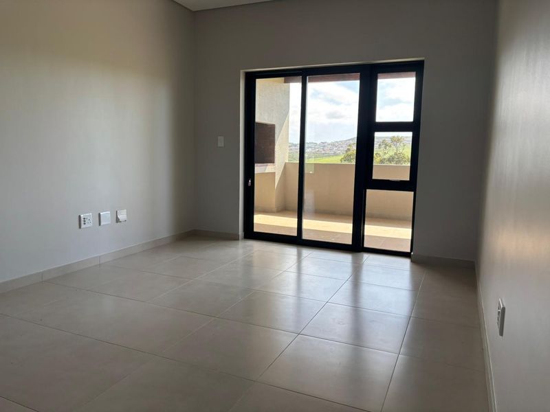 A bright, empty bedroom featuring neutral tiled flooring and a large sliding glass door providing access to an outdoor balcony.
