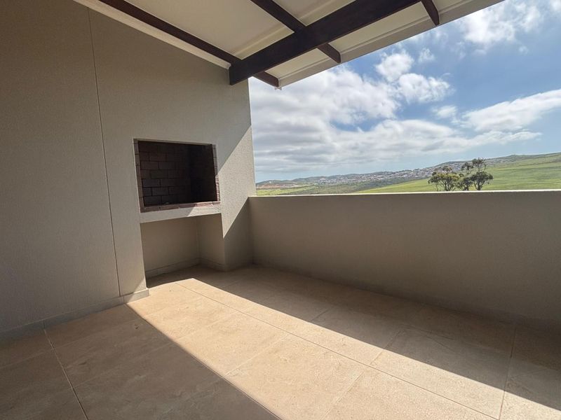 A spacious covered balcony featuring a built-in braai and scenic landscape views, offering an ideal space for outdoor entertaining.