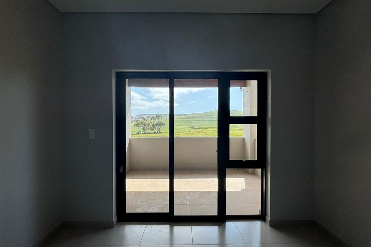 An empty, modern living area featuring neutral tiled floors and a large sliding glass door that opens onto a balcony with scenic landscape views.