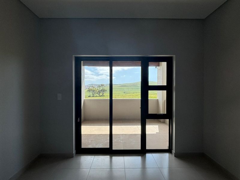 An empty, modern living area featuring neutral tiled floors and a large sliding glass door that opens onto a balcony with scenic landscape views.