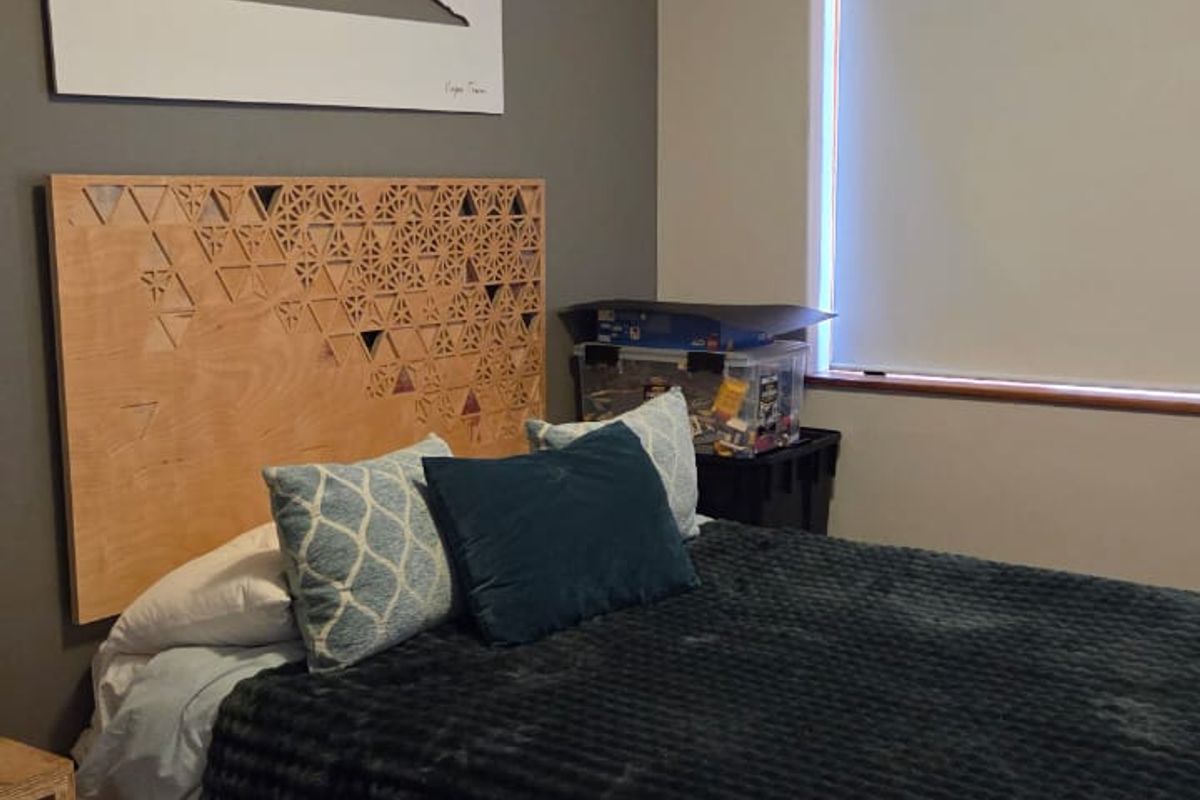 A well-maintained bedroom featuring laminate flooring, a neutral color palette, and a roller blind for privacy.