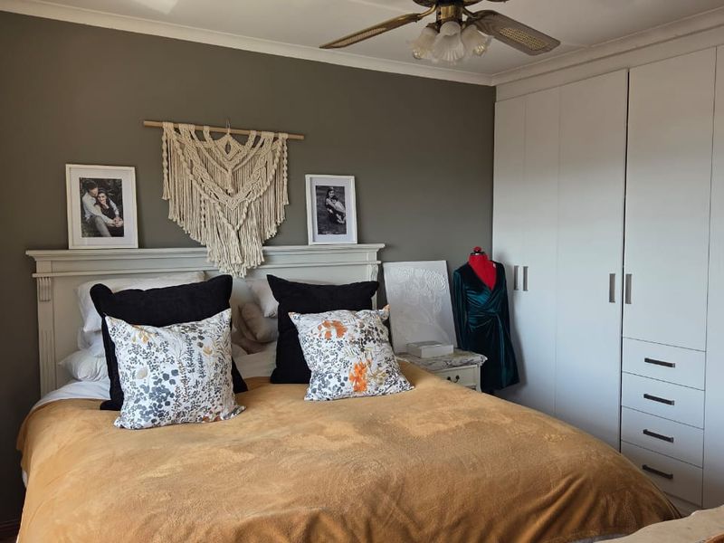 A well-maintained bedroom featuring ample built-in cupboard storage and a ceiling fan, finished with neutral wall tones and classic coving.