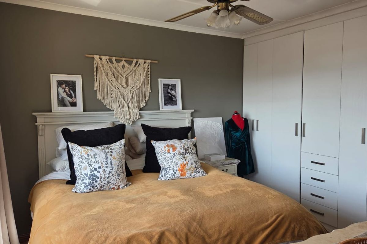 A well-maintained bedroom featuring ample built-in cupboard storage and a ceiling fan, finished with neutral wall tones and classic coving.