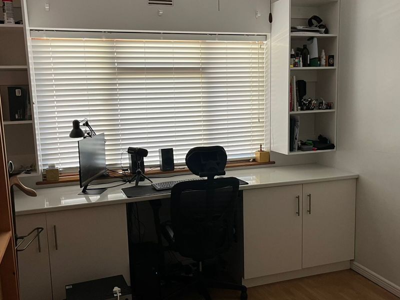 A functional home office featuring built-in desk space, integrated cabinetry, and shelving, complemented by venetian blinds and laminate flooring.