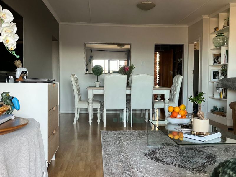 An open-plan living and dining area featuring laminate flooring, a built-in shelving unit, and coved ceiling details.