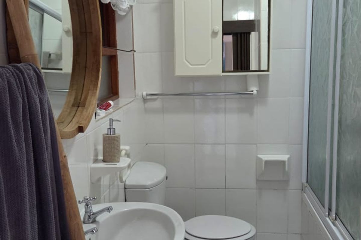 A functional bathroom featuring a pedestal basin, toilet, and a shower enclosure with tiled walls and flooring throughout.