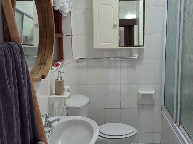 A functional bathroom featuring a pedestal basin, toilet, and a shower enclosure with tiled walls and flooring throughout.