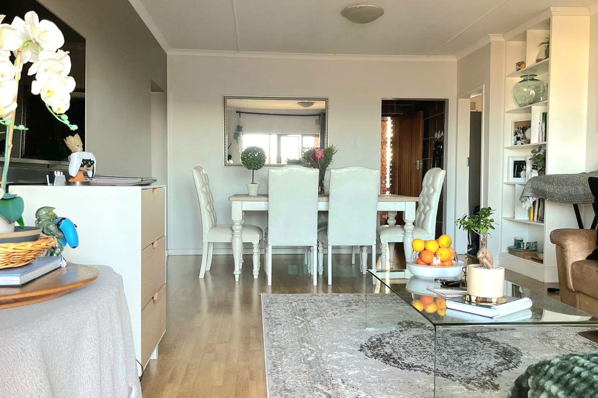 An open-plan living and dining area featuring laminate flooring and a built-in shelving unit, creating a functional and connected living space.