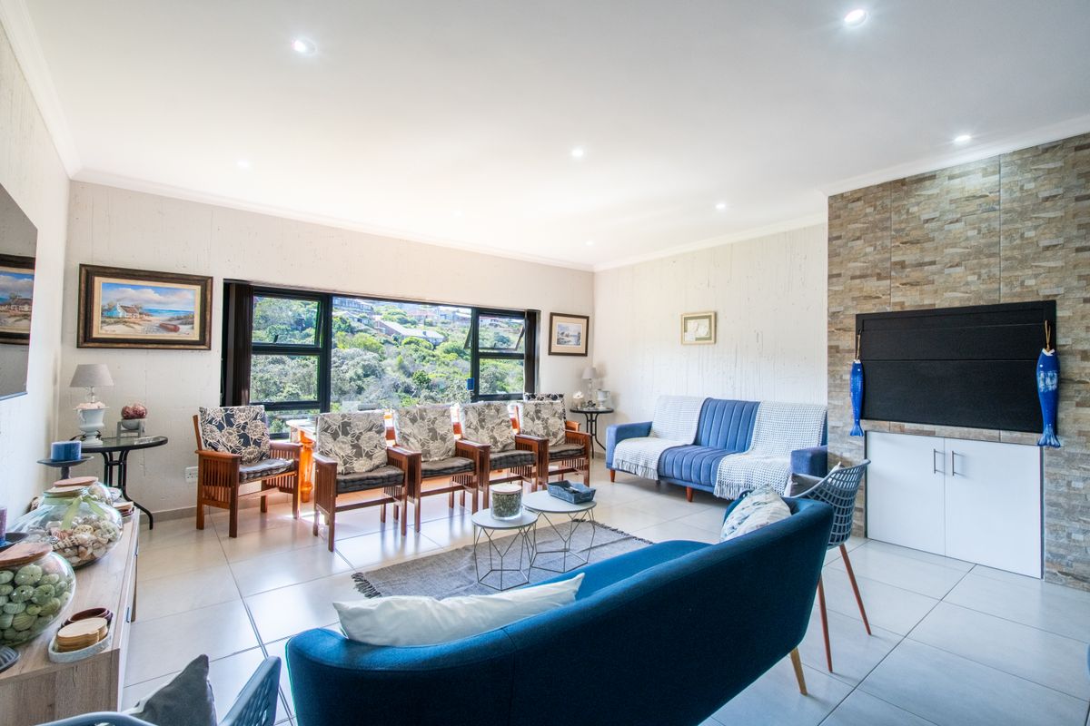 Spacious living room featuring tiled floors, recessed lighting, and a stone-clad feature wall with built-in cabinetry, offering pleasant views through large windows.