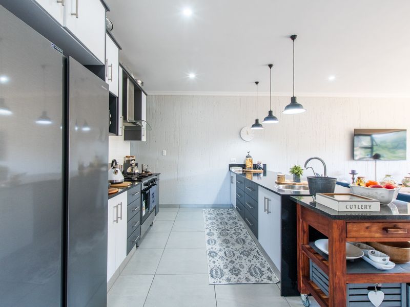 Modern open-plan kitchen featuring sleek two-tone cabinetry, a central island with a sink, integrated appliances, and contemporary pendant lighting.