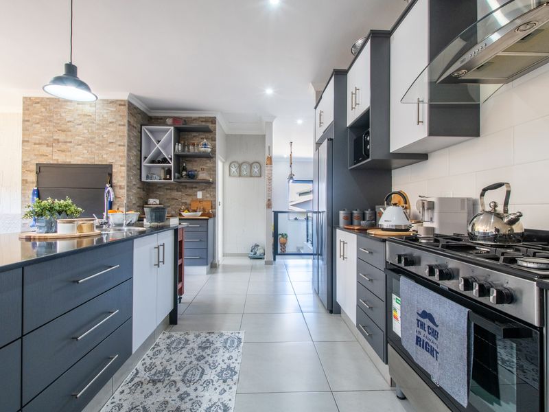 Modern kitchen featuring dark and light cabinetry, a central island, stone countertops, gas stove with extractor, and tiled flooring.