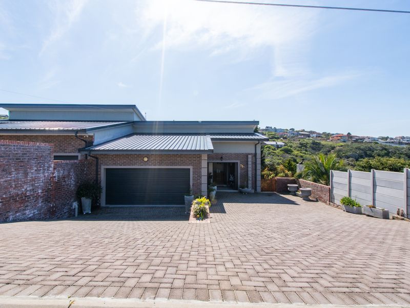 Front elevation of a modern duet property featuring a brick facade, metal roof, double garage, and a spacious paved driveway.