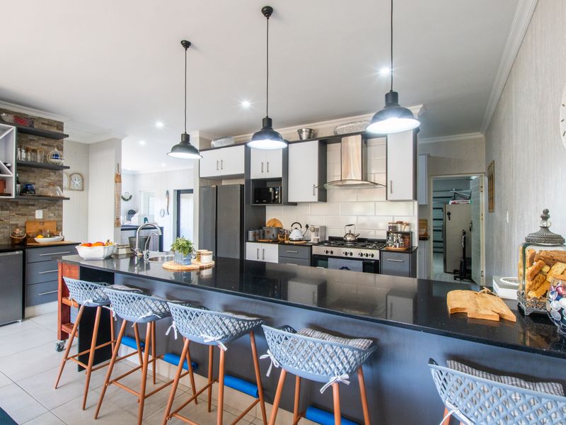 Modern kitchen featuring a large granite island, gas hob, extractor fan, and stylish pendant lighting, complemented by a stone-clad feature wall.