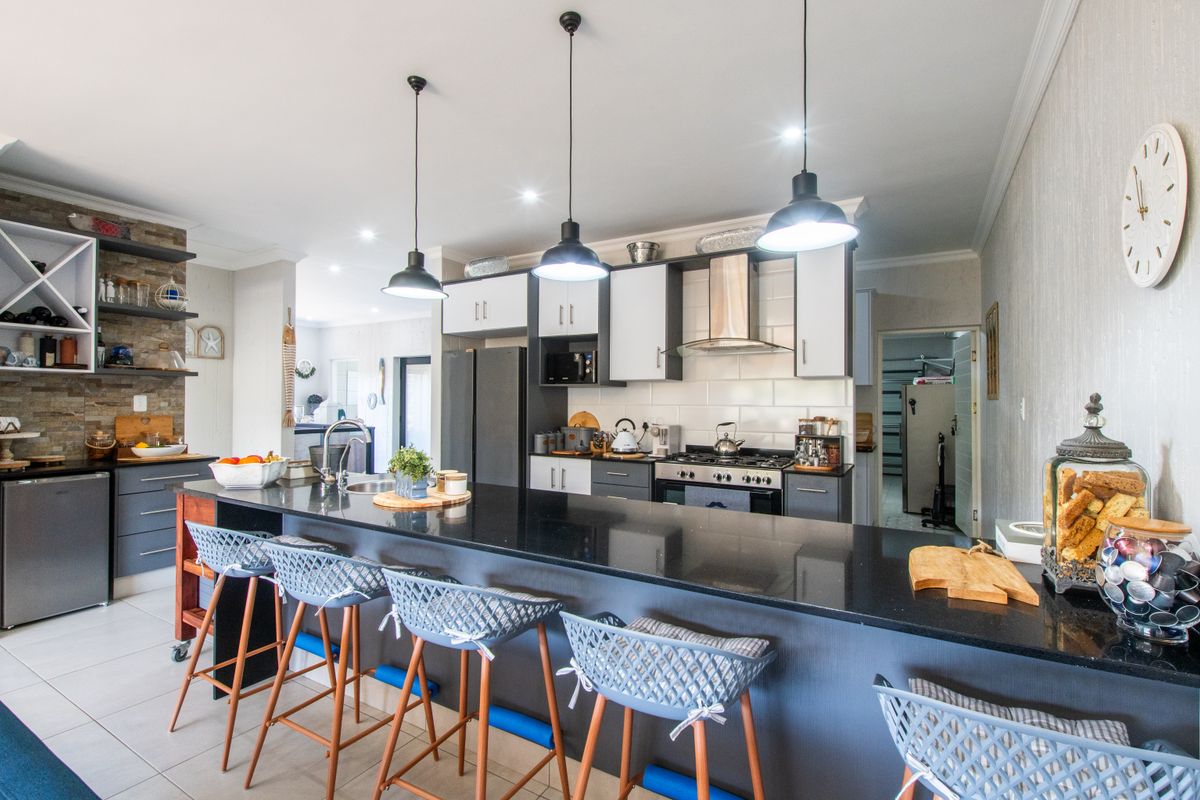 Modern kitchen featuring a large granite island, gas hob, extractor fan, and stylish pendant lighting, complemented by a stone-clad feature wall.