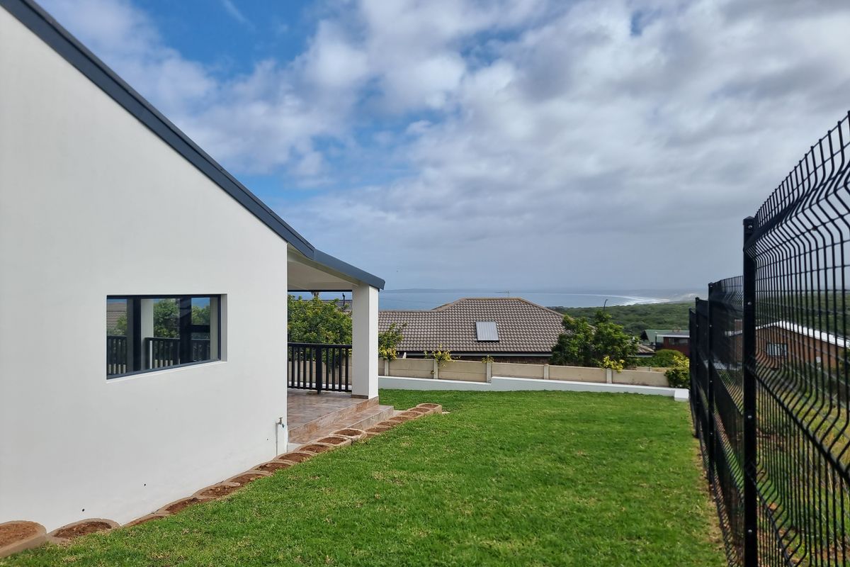 Rear view of the property featuring a covered patio, well-maintained lawn, and perimeter fencing with distant coastal views.