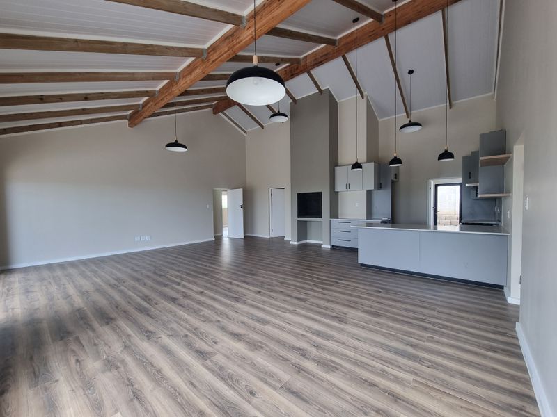 Spacious open-plan living area featuring vaulted ceilings with exposed timber beams, modern kitchen cabinetry, a built-in fireplace, and durable laminate flooring.