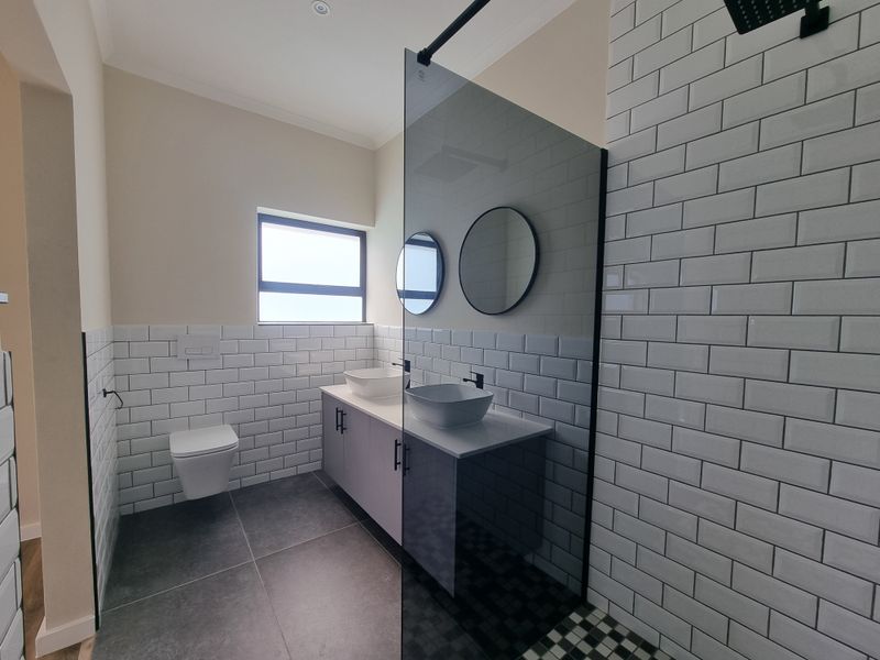 Modern bathroom featuring a double vanity with vessel sinks, wall-hung toilet, subway tile finishes, and a spacious walk-in shower with a glass screen.