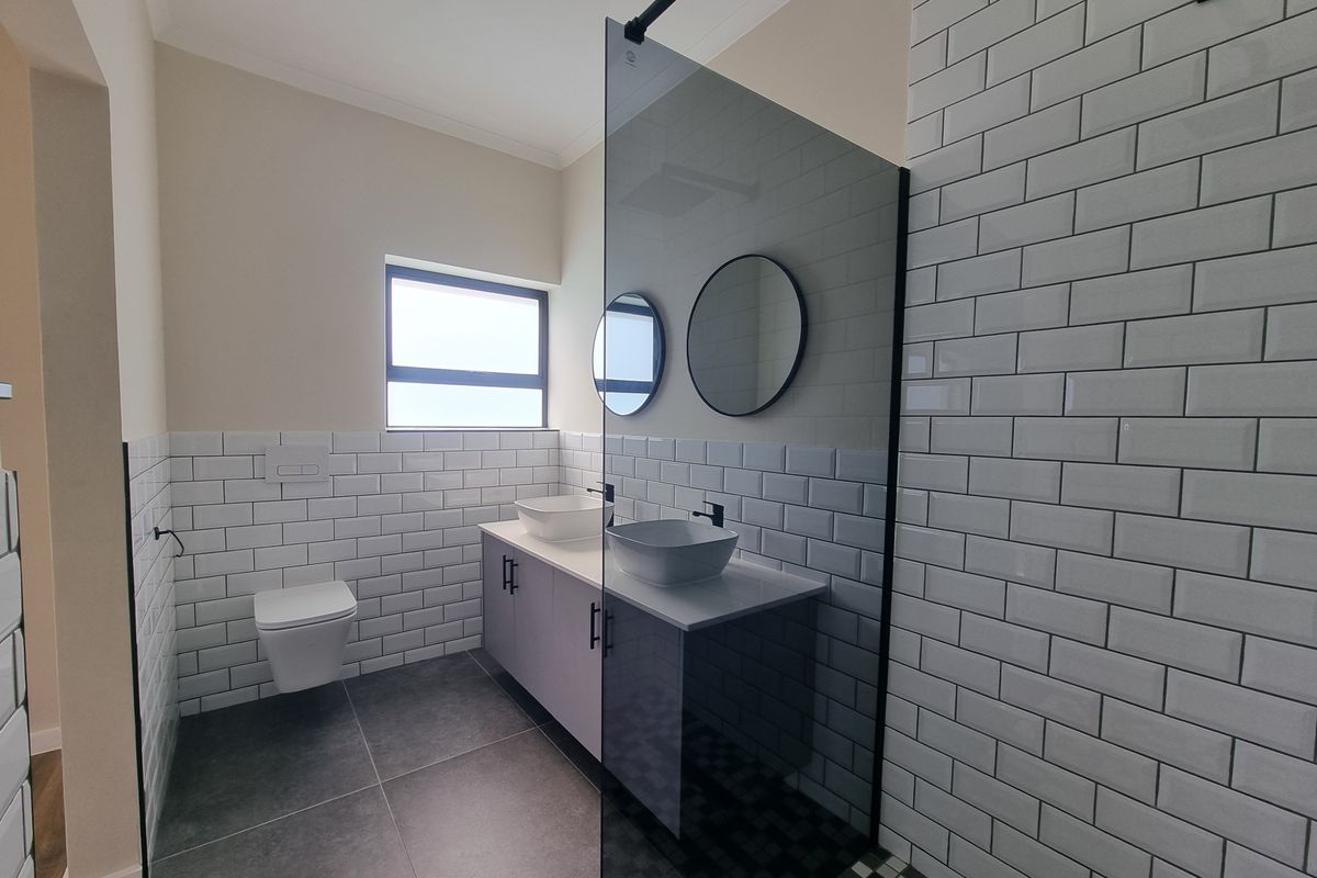 Modern bathroom featuring a double vanity with vessel sinks, wall-hung toilet, subway tile finishes, and a spacious walk-in shower with a glass screen.