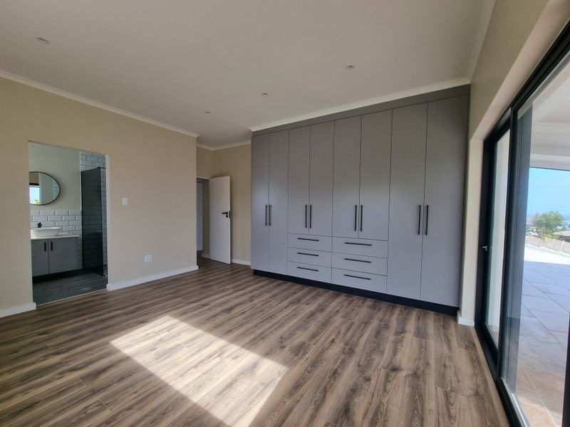 Spacious bedroom featuring modern grey built-in cupboards, laminate flooring, recessed lighting, and sliding glass doors leading to an outdoor area with en-suite access.