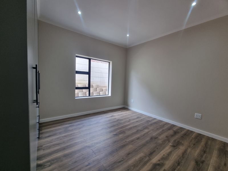 A clean, modern bedroom featuring neutral walls, durable laminate flooring, recessed lighting, and built-in storage cupboards.