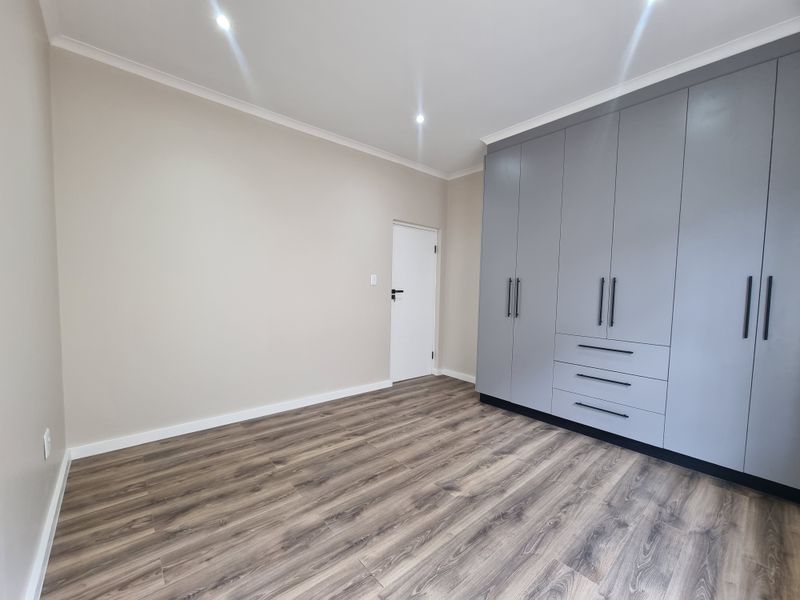 A bright, modern bedroom featuring neutral walls, high-quality laminate flooring, and extensive grey built-in cupboards with contemporary black hardware.