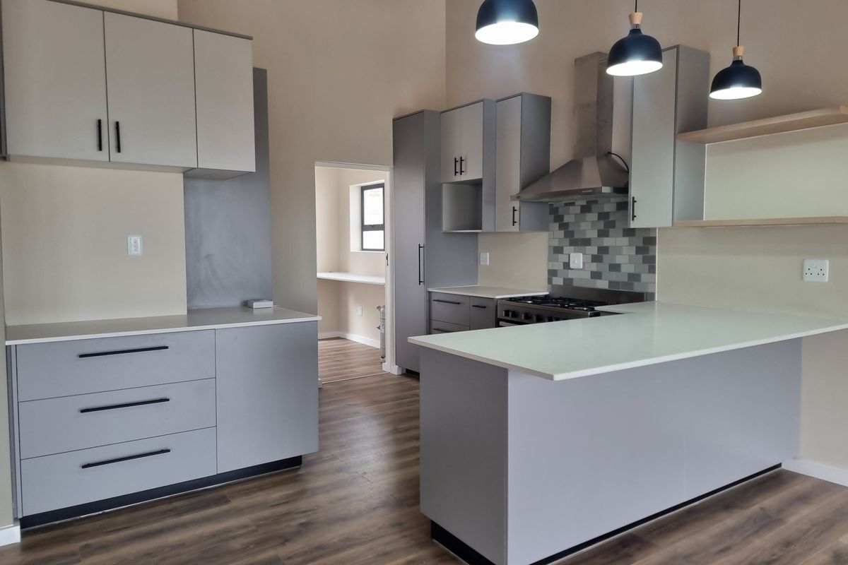 Modern kitchen featuring sleek grey cabinetry, stone countertops, gas hob with extractor fan, and durable laminate flooring, leading into a secondary utility space.
