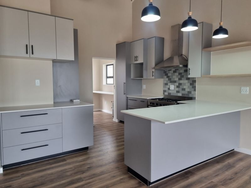 Modern kitchen featuring sleek grey cabinetry, stone countertops, gas hob with extractor fan, and durable laminate flooring, leading into a secondary utility space.