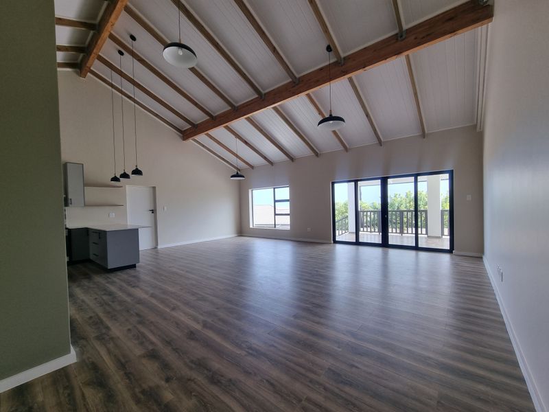 Spacious open-plan living area featuring vaulted ceilings with exposed timber beams, modern laminate flooring, and large sliding doors leading to an outdoor patio.