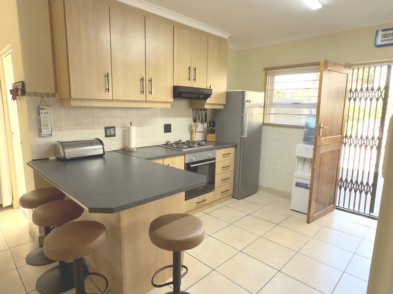 Functional kitchen featuring light wood cabinetry, gas hob, under-counter oven, breakfast nook, and direct access to the exterior via a security gate.