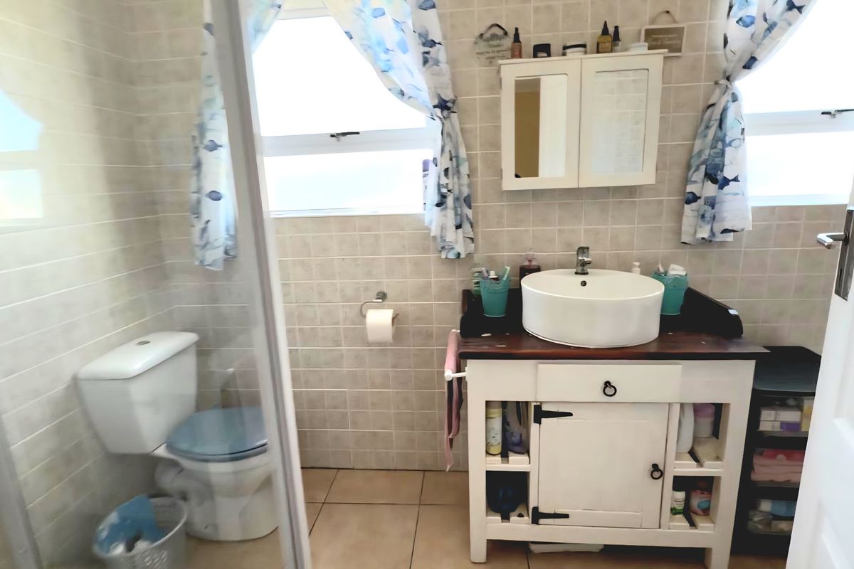 A functional bathroom featuring a vessel sink vanity, toilet, and a glass-enclosed shower with neutral wall and floor tiling.