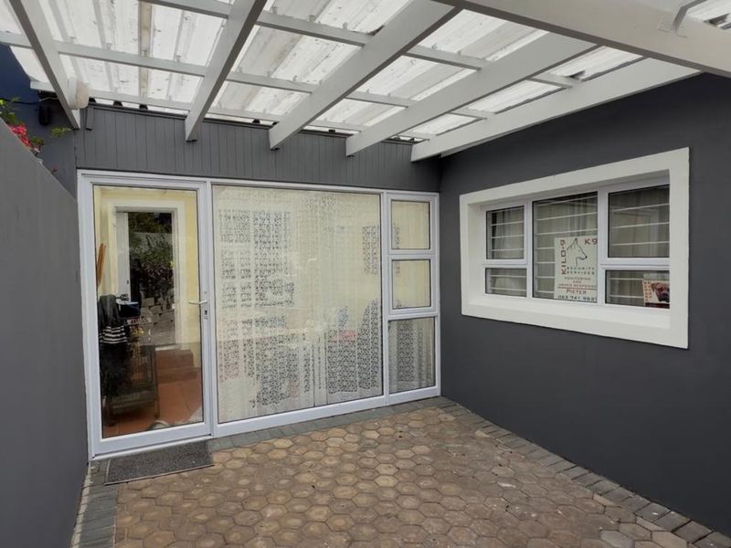 A covered patio area featuring paved flooring, a white pergola structure, and access to the interior through a sliding glass door.