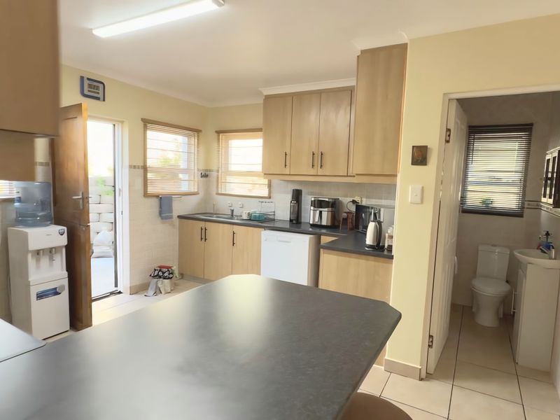 Functional kitchen featuring laminate cabinetry, dark countertops, tiled backsplash, and direct access to an adjacent bathroom and outdoor area.