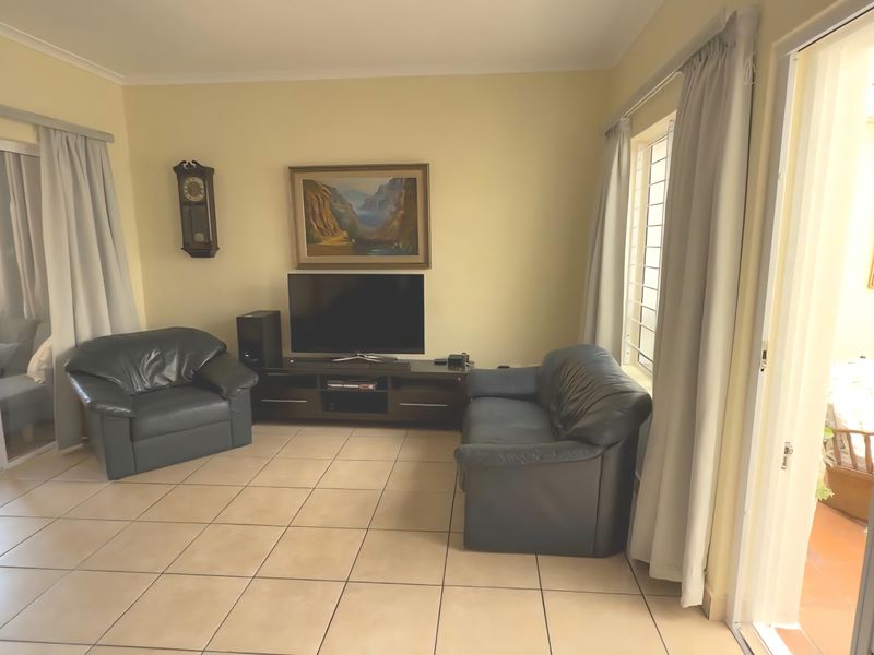 A living room featuring neutral tiled flooring, sliding glass doors leading to an outdoor area, and security bars on the windows.
