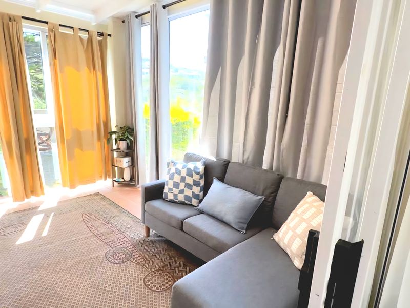 A bright living room featuring expansive glass windows and sliding doors that provide ample natural light and views of the surrounding greenery.