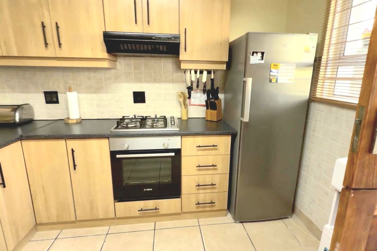 A functional kitchen featuring light wood cabinetry, dark laminate countertops, a gas hob, built-in oven, and tiled finishes throughout.