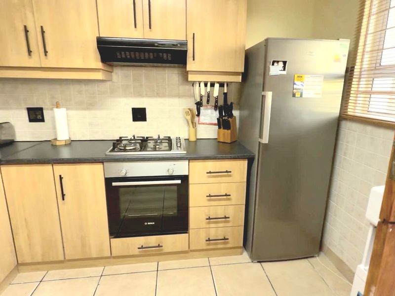 A functional kitchen featuring light wood cabinetry, dark laminate countertops, a gas hob, built-in oven, and tiled finishes throughout.