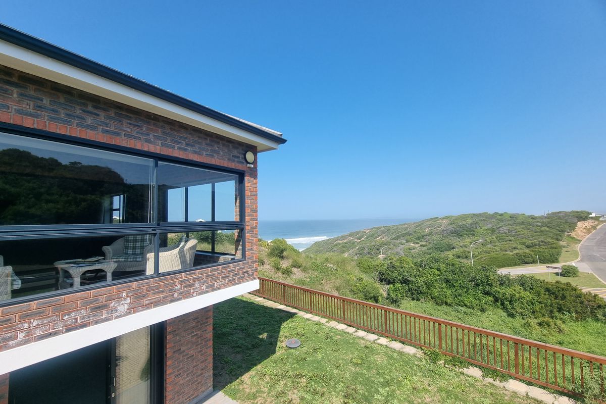 Rear view of a brick house featuring large glass windows and a wooden balustrade overlooking a coastal landscape.