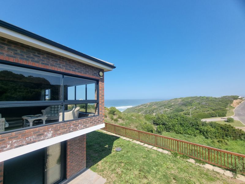 Rear view of a brick house featuring large glass windows and a wooden balustrade overlooking a coastal landscape.