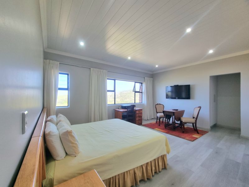 Spacious bedroom featuring modern laminate flooring, recessed downlighting, and a tongue and groove ceiling with large windows offering natural light.
