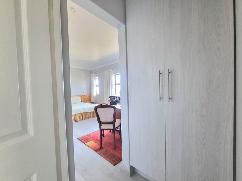 A view from the hallway into a bedroom featuring light wood-look built-in cupboards, laminate flooring, and a classic tongue and groove ceiling.