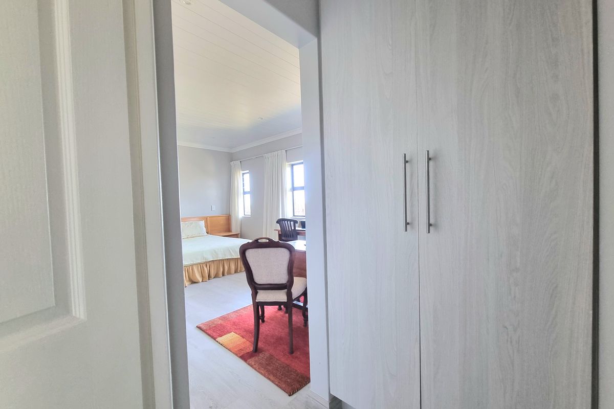 A view from the hallway into a bedroom featuring light wood-look built-in cupboards, laminate flooring, and a classic tongue and groove ceiling.