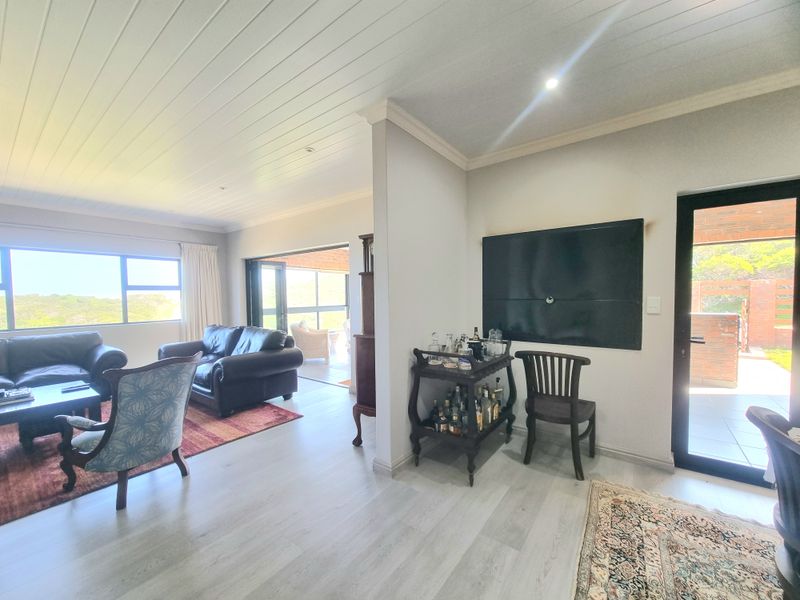 Spacious living area featuring light laminate flooring, tongue and groove ceiling, and large windows providing natural light and access to the outdoor patio.