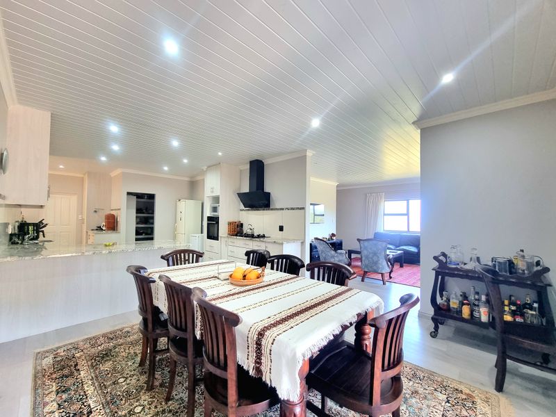 Spacious open-plan living area featuring a modern kitchen with island, built-in appliances, and a bright dining space under a stylish tongue and groove ceiling.