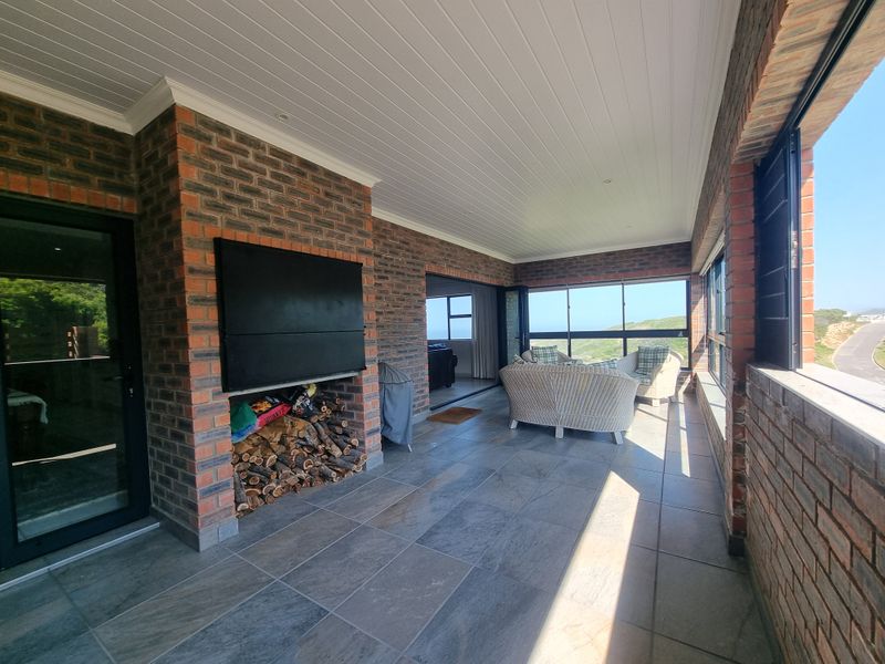 Spacious covered patio featuring exposed brick walls, tiled flooring, and a built-in fireplace, offering an ideal space for outdoor entertaining with scenic views.