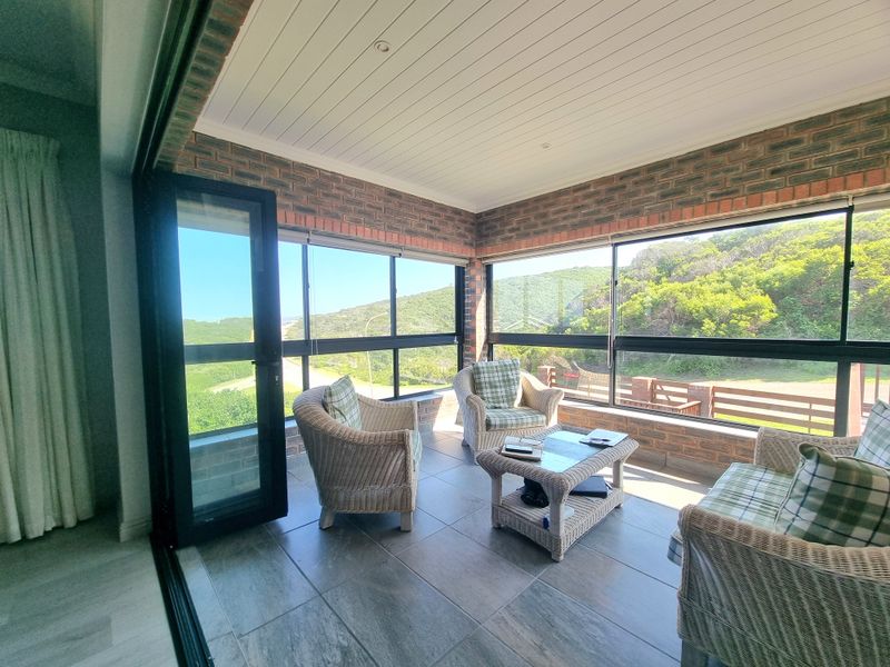 A bright, enclosed patio featuring exposed brick walls, tiled flooring, and large glass windows offering scenic views of the surrounding landscape.