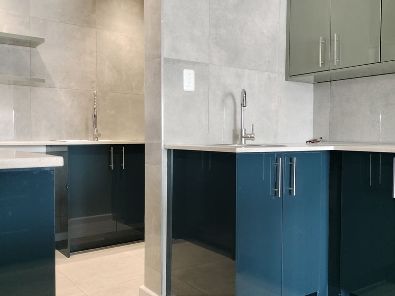 Modern kitchen featuring high-gloss blue cabinetry, stone countertops, tiled splashbacks, and integrated sink fixtures in a clean, contemporary layout.