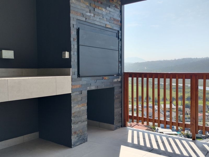 Covered balcony featuring a built-in braai with stone cladding, stone countertop, and wooden balustrade, offering scenic elevated views.