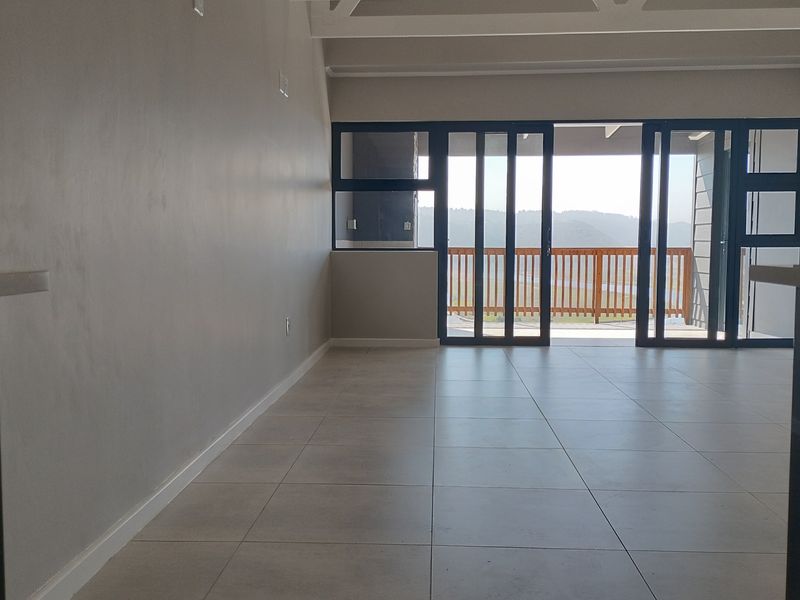 Spacious open-plan living area featuring neutral tiled flooring, exposed ceiling beams, and large sliding glass doors leading to an outdoor balcony.