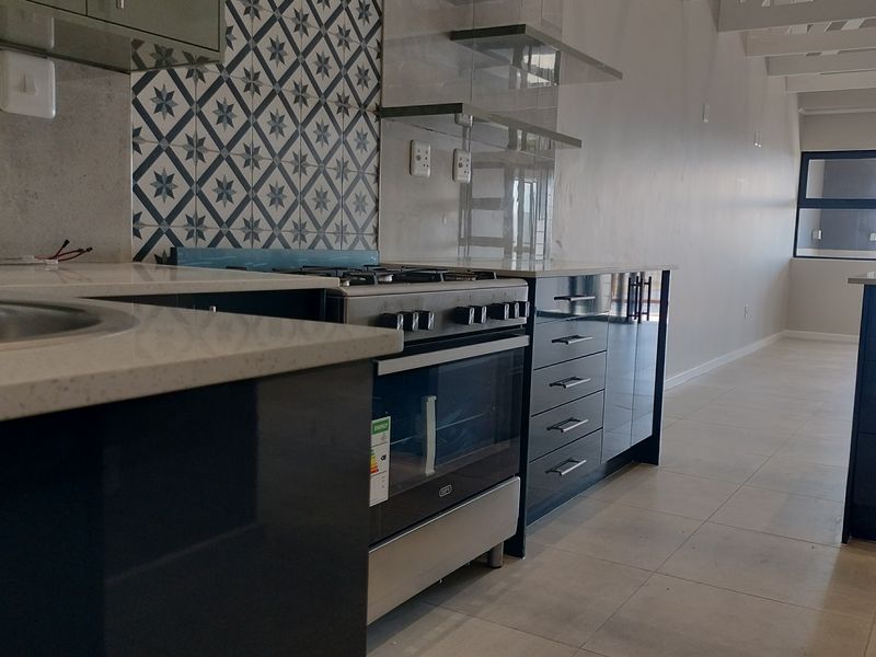Modern kitchen featuring dark cabinetry, quartz countertops, a gas stove, and decorative tile backsplash, set within an open-plan living space.