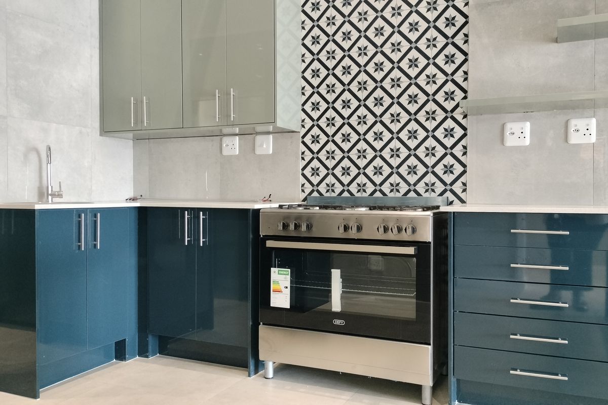 Modern kitchen featuring high-gloss blue cabinetry, stone countertops, a patterned tile splashback, and a stainless steel freestanding oven.